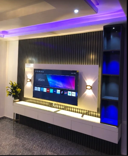 Media wall with a television, dark fluted panels, white console and purple ceiling lighting